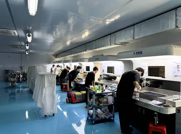 Operators work on small pieces at illuminated machine stations, with trays and materials beside them.