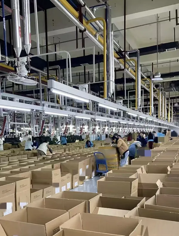 Open cartons are arranged across a work area, with operators working between the boxes and the production line.