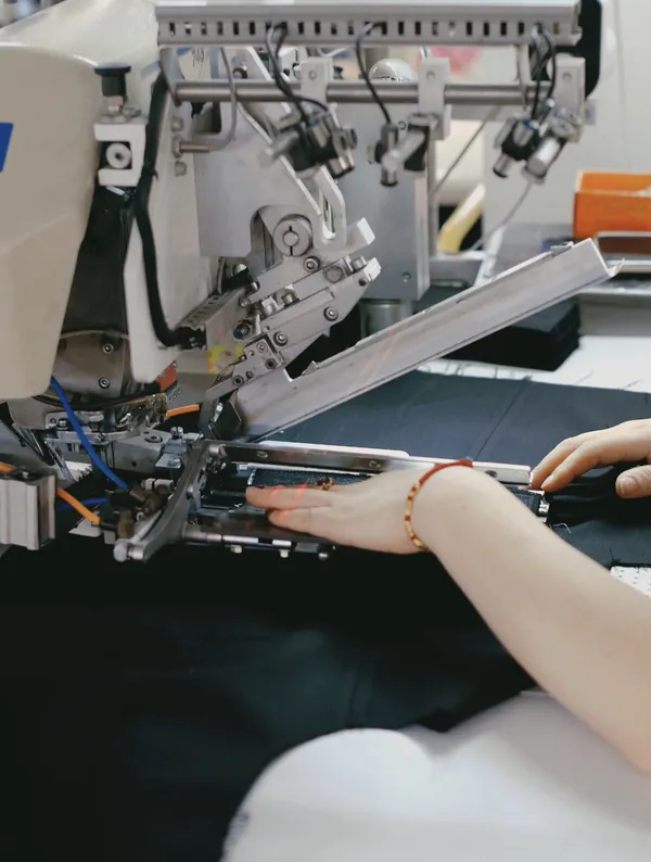 An operator positions dark fabric at a sewing machine, showing the hands and machine components in close view.