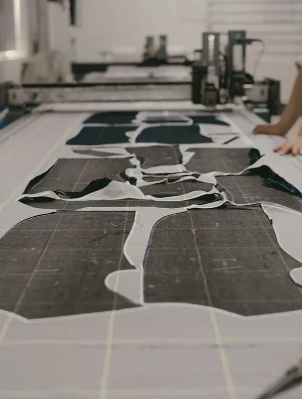 Fabric panels of different shapes are laid across a cutting table, with cutting equipment visible behind them.