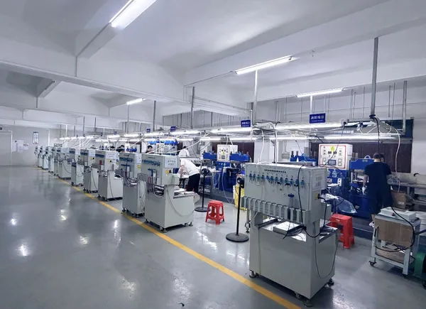 Rows of machines and workstations line the workshop, with operators and containers beside the aisle.